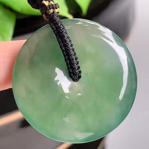 Pu&ograve; includere: Un ciondolo rotondo in giada verde chiaro con un cordoncino nero. Il ciondolo &egrave; liscio e lucido.