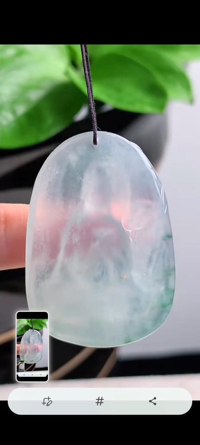 May include: A jade pendant with a rounded shape, suspended from a black cord. The jade features a blend of pale green, white, and hints of pink. The pendant is smooth and polished, reflecting light.