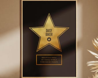 Puede incluir: Impresión enmarcada con fondo negro y detalles dorados. El diseño presenta una estrella dorada con el nombre "DAISY BAKER" y una estrella más pequeña en el centro. Debajo, un rectángulo dorado con texto. Las palabras "DIGITAL FILE" están en la parte inferior.