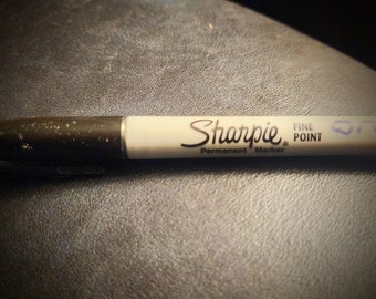 Könnte beinhalten: Ein schwarz-weißer Sharpie Fine Point Permanentmarker mit schwarzer Kappe und weißem Schaft. Der Schaft trägt den schwarzen Schriftzug Sharpie Permanent Marker Fine Point und eine kleine blaue handschriftliche Markierung nahe der Spitze.