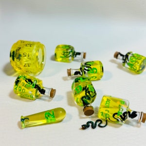 May include: A set of eight yellow dice with green and black markings. The dice are shaped like bottles and have a snake design. The dice are numbered 1 through 6.