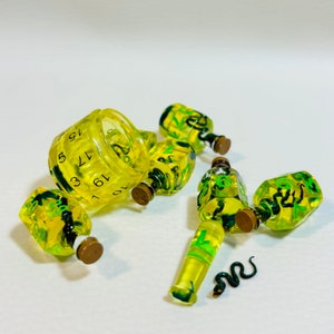 May include: A set of yellow and green dice with snake designs. The dice are shaped like bottles and have numbers on them. One die is a d10 and has a ring shape.