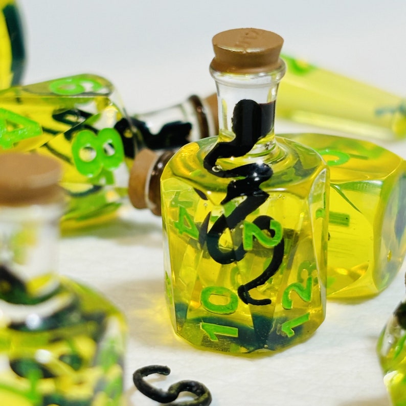 May include: A set of six clear glass bottles with cork tops filled with a yellow liquid. The bottles are decorated with black and green paint and numbers.