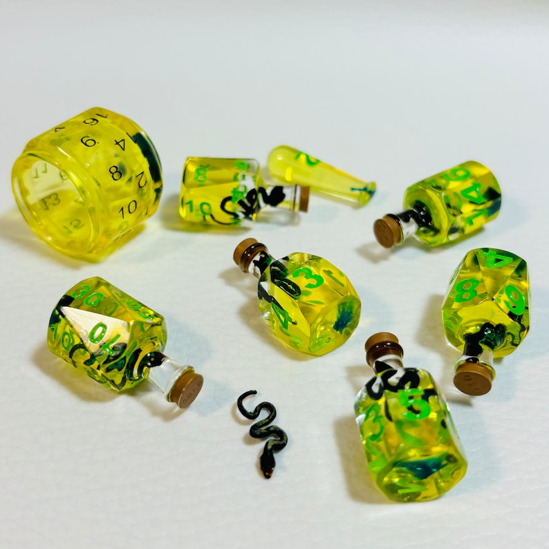 May include: A set of 10-sided dice with a snake theme. The dice are made of clear resin with green and black accents. The dice are shaped like bottles and have numbers 1-10 on the sides. The dice are perfect for tabletop games.