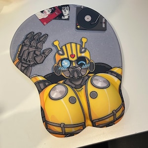 Pode incluir: Um robô de desenho animado amarelo e preto com um coração no peito, usando uma viseira azul e um capacete preto. O robô está sentado em um fundo cinza com um toca-discos e um disco no fundo.