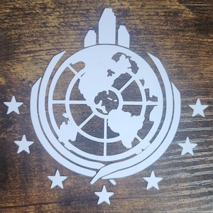May include: White silhouette of a globe with a city skyline on top, surrounded by eight stars, on a brown wooden background.