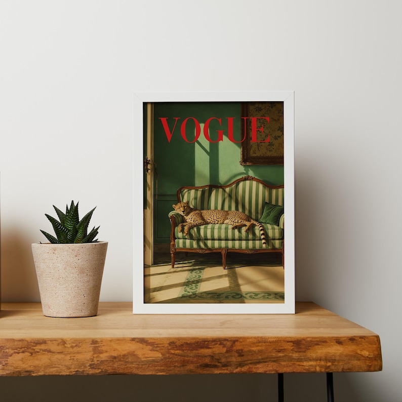 K&ouml;nnte beinhalten: Ein gerahmter Wandkunstdruck, der einen Geparden auf einem gr&uuml;n-wei&szlig; gestreiften Sofa in einem Raum mit gr&uuml;nen W&auml;nden zeigt. Das Wort VOGUE ist oben in roten Gro&szlig;buchstaben gedruckt. Eine kleine gr&uuml;ne Sukkulente in einem beigen Topf steht daneben.