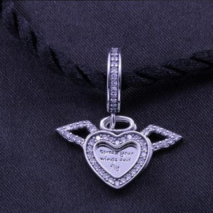 May include: A silver heart-shaped pendant with wings, encrusted with small, clear stones. The pendant has the words "Spread your wings and fly" engraved on it. The pendant hangs from a silver loop.