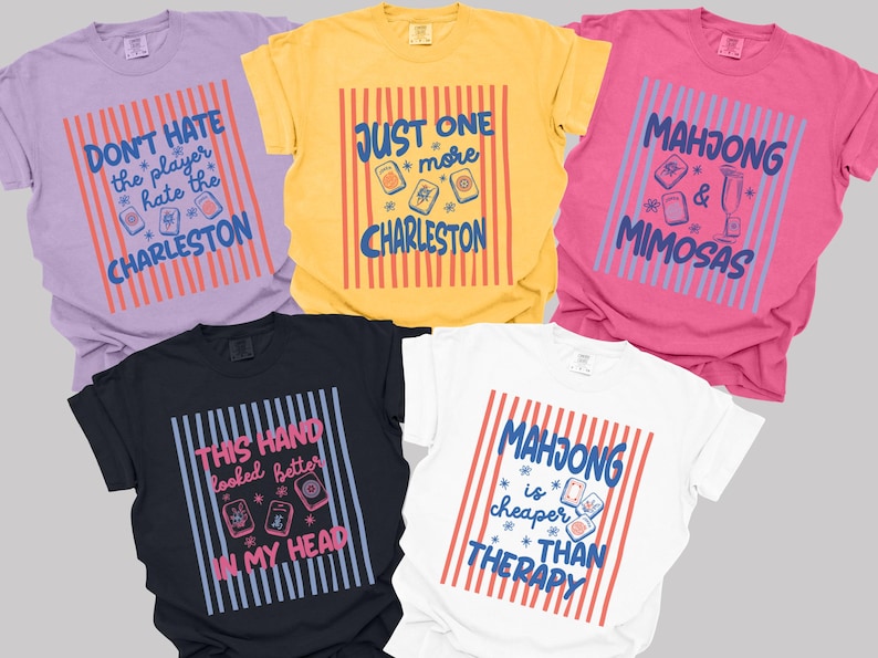 May include: Five short-sleeved crew neck t-shirts in lavender, yellow, pink, black, and white. Each shirt features a central graphic with vertical stripes and text including phrases like Don't Hate the Player Hate the Charleston and Mahjong is Cheaper than Therapy.