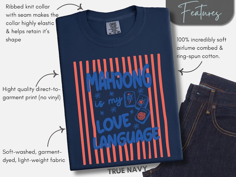 May include: A true navy blue t-shirt featuring a graphic print with vertical coral stripes and the blue text "MAHJONG is my LOVE LANGUAGE" accompanied by three mahjong tile illustrations and small star-like floral accents on the front.