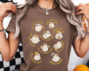 May include: Brown t-shirt featuring a Halloween-themed design with cartoon ghosts and phrases like "Boo-tiful Minds at Work" and "Spook-tacular Students." The ghosts are adorned with flowers and pumpkins.