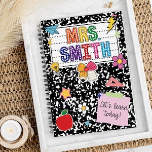 May include: Spiral-bound notebook with a black and white speckled cover. The notebook features the text "MRS. SMITH" in colorful letters, along with various school-themed stickers, including a lightbulb, apple, and flower. A pink sticky note reads "Let's learn today!"