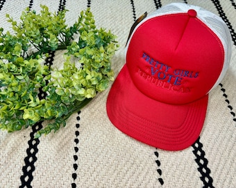May include: Red and white trucker hat with a blue embroidered message that reads "Pretty Girls Vote Republican".