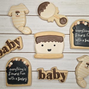 May include: Assortment of baby-themed cookies, including a onesie, rattle, and cookies with the word "baby". One cookie features a smiling s'more design. Two cookies have the text "everything is s'more fun with a Baby".