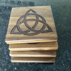 May include: Set of four wooden coasters featuring a laser-etched Celtic knot design. The coasters are made of dark brown wood and have a smooth, polished finish.