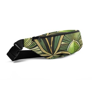 May include: A fanny pack with a tropical leaf pattern in shades of green and gold. The bag has a black adjustable strap with a buckle closure and a black zipper. The design features large, stylized leaves and geometric shapes.