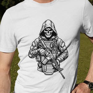 Puede incluir: Camiseta blanca con una ilustraci&oacute;n en blanco y negro de una calavera con capucha en equipo t&aacute;ctico, sosteniendo un rifle. El dise&ntilde;o incluye un chaleco, granadas y sombreado detallado.