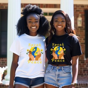 Peut inclure: Deux personnes portant des t-shirts blancs et noirs avec un graphique de mains tenant un globe et le texte "Speak Peace".