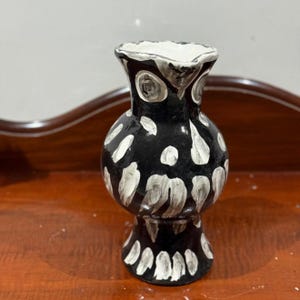 Peut inclure: Un vase en céramique noire fait à la main avec des motifs abstraits blancs. Le vase a un corps bulbeux et un bord évasé et ondulé. L'intérieur est blanc et le vase repose sur une surface en bois. Une pièce décorative pour la maison.