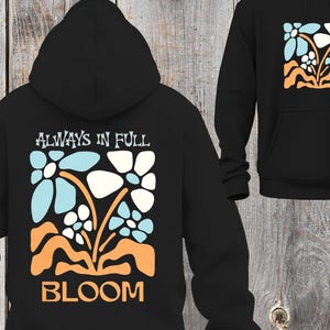 May include: Black hoodie with a floral design in light blue, white, and orange. The back of the hoodie features the text "ALWAYS IN FULL BLOOM" above the floral graphic. The front of the hoodie has a smaller version of the floral design.