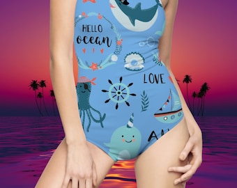 Pode incluir: Um maiô azul com tema náutico apresentando um tubarão, um polvo, um narval e um veleiro. O maiô tem o texto "Hello Ocean" e "Love" impresso.