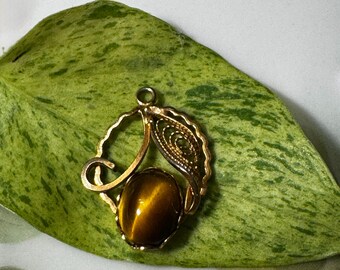 May include: Gold pendant with a brown tiger's eye stone set in a filigree design.
