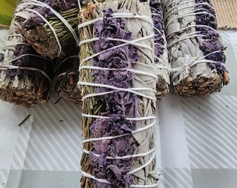 Puede incluir: Varios manojos de hierbas secas, incluyendo salvia y lavanda, están atados con hilo blanco. La salvia es de un color gris verdoso pálido, y la lavanda es de un púrpura intenso. Los manojos están dispuestos sobre una superficie a cuadros.