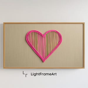 May include: A pink heart-shaped wall art piece made of yarn, with a light brown wooden frame. The heart is made of pink yarn with a multi-colored yarn pattern inside. The frame has the text "LightFrameArt" printed on the bottom.