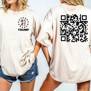 May include: A white t-shirt with a black and red design of the numbers 45 and 47 with stars and the word "TRUMP" on the front. The back of the shirt has a black and white QR code.