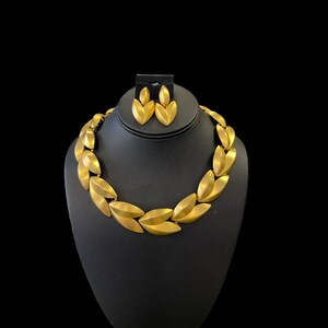 May include: A gold-tone necklace and earrings set featuring a leaf design. The necklace is made of linked leaf-shaped pieces and the earrings are simple, single leaf designs.