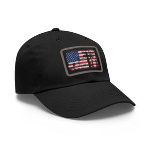 Op de afbeelding: Zwarte baseballpet met een versleten Amerikaanse vlag patch. De patch heeft een rechthoekige vorm met een grijze rand, met de sterren en strepen in rood, wit en blauw. De pet heeft een gebogen klep en een gestructureerde kroon.