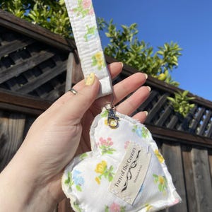 May include: A white heart-shaped keychain with a floral pattern and a tag that reads "Turn of the Century" and "Handmade in USA".