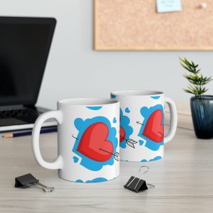 May include: Two white ceramic mugs featuring a red heart with an arrow through it on a blue cloud pattern.