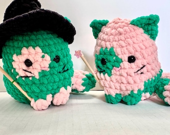 May include: Two crocheted plush cat toys. One is green and pink with a black witch hat. The other is pink and green. Both have black eyes and whiskers.
