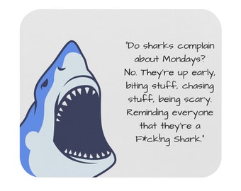 May include: A white mousepad with a cartoon shark graphic. The shark is blue and white with an open mouth. Text on the mousepad reads: "Do sharks complain about Mondays? No. They're up early...F*ck!ng Shark."