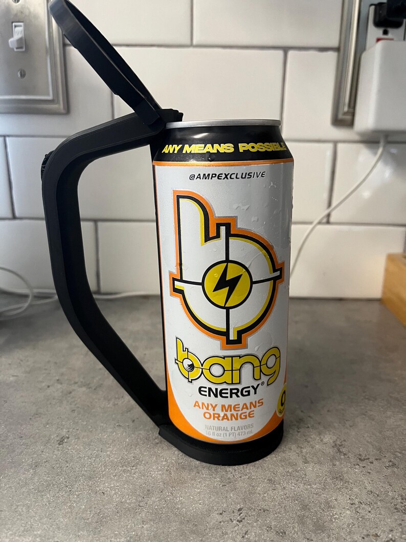 May include: A black can holder with a black handle is attached to a white and orange Bang Energy drink can. The can features the text "ANY MEANS POSSIBLE" and "ANY MEANS ORANGE". The can has a yellow lightning bolt design.