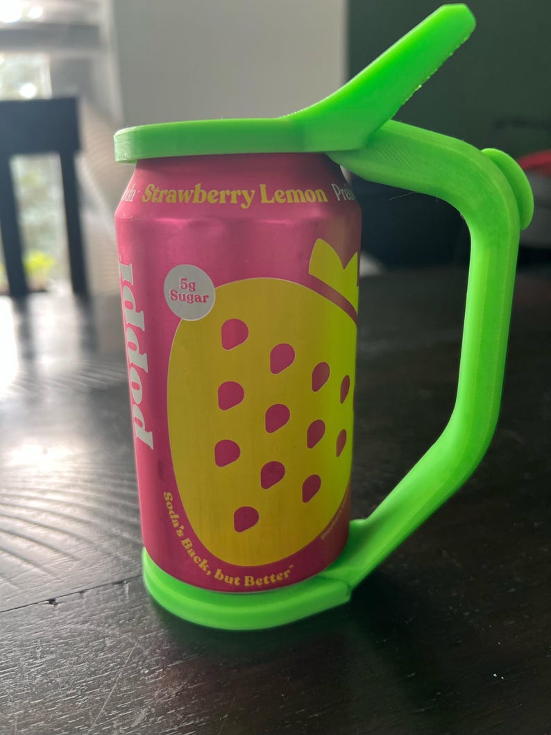May include: A pink can of "Poppi" soda with a yellow strawberry graphic and the text "Strawberry Lemon Pre". A bright green handle and lid are attached to the can. The can also has the text "Soda's Back, but Better".