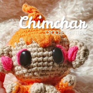 May include: A crocheted Chimchar doll with orange and tan yarn. The doll has black eyes, pink accents, and the text "Chimchar CROCHET PATTERN". The doll is held in a hand.