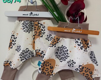 Könnte beinhalten: Zwei Paar braune und weiße Babyhosen mit Leopardenmuster. Die Hosen hängen an Holzbügeln mit dem Text "met Tejohl" darauf. Die Größen sind 68/74 und 56/62.