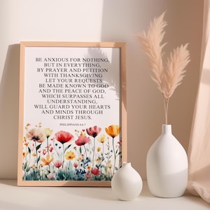 May include: A framed print with a floral watercolor design and the text "BE ANXIOUS FOR NOTHING..." in black. The print is in a light wood frame. A white vase with pampas grass and a small white vase are on a white surface.