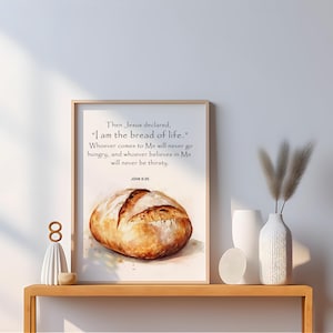 Può includere: Una stampa incorniciata con il testo "Io sono il pane della vita" e un acquerello di una pagnotta di pane. La stampa è esposta su una mensola di legno con oggetti decorativi.
