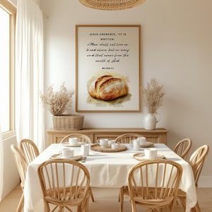 Op de afbeelding: Een ingelijst print met een aquarel van een brood en een bijbelvers dat luidt: "Jezus antwoordde: "Er staat geschreven: 'De mens zal niet van brood alleen leven, maar van elk woord dat uit de mond van God komt.'" Mattheüs 4:4
