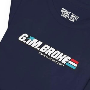 May include: A navy blue t-shirt with a white graphic that says "G.M. BROKE BANK ACCOUNT ZERO" with a red, white, and blue stripe design. The text "BROKE BOYZ SOCIETY CLUB" is printed on the neck tag.
