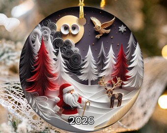 May include: A round ceramic Christmas ornament featuring a quilling-style paper art design of a winter forest with red and white trees, a Santa Claus figure, a reindeer, and an owl under a moon. The year 2026 is printed in black at the bottom.