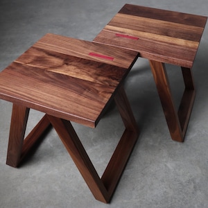 May include: Two wooden end tables with a triangular base and a square top. The tables are made of dark brown wood and have a red accent on the top.