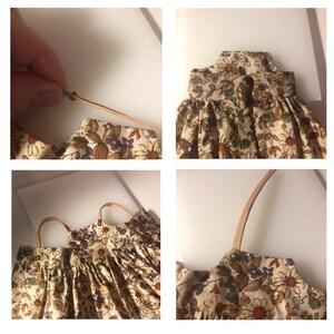 May include: A miniature floral print dress with tan straps. The dress features a beige background with brown, purple, and green floral patterns. The straps are a light brown color. The dress is likely for a doll or small figurine.