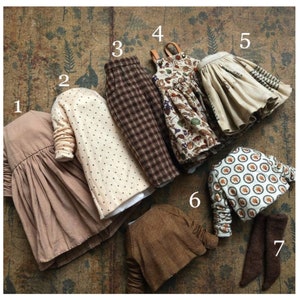 May include: A collection of doll clothes in various styles and patterns. Includes a tan dress, a cream-colored jacket with black polka dots, brown plaid pants, a floral print dress, a tan skirt, a patterned jacket, and brown leggings.