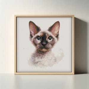May include: A framed print featuring a detailed portrait of a Devon Rex cat. The cat has large, expressive eyes, a brown face, and large ears. The artwork is set against a white background, framed in a light wood frame.