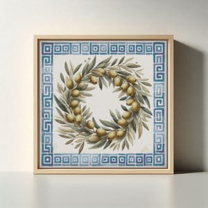 May include: Square framed artwork depicting an olive wreath with green leaves and golden olives. The wreath is centered on a white background, framed by a blue and white Greek key border. The frame is a light wood colour.