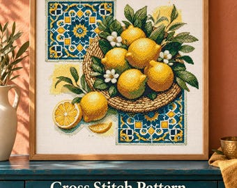 May include: A framed cross stitch pattern featuring a woven basket filled with bright yellow lemons and green leaves, accented by white blossoms. The design includes blue and yellow geometric tile patterns and a sliced lemon.